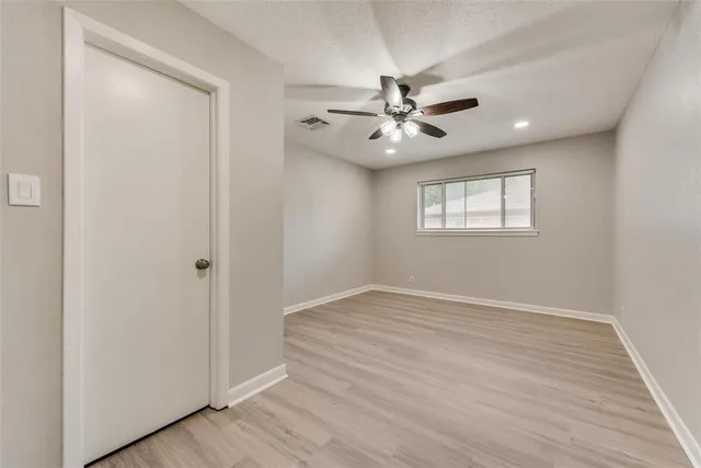 an empty room with wooden floor fan and windows