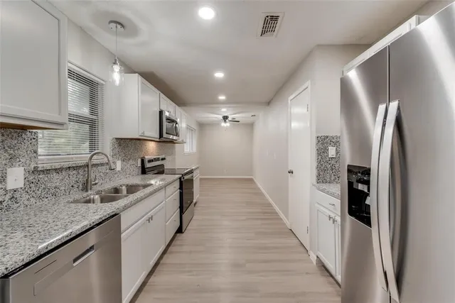 a large kitchen with stainless steel appliances sink a refrigerator and a counter top space