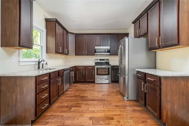 a kitchen with stainless steel appliances granite countertop a refrigerator a sink a stove and wooden cabinets