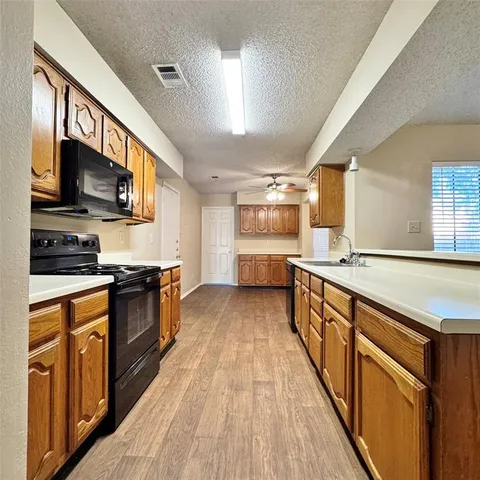a large kitchen with stainless steel appliances granite countertop a stove top oven a sink dishwasher and a refrigerator with wooden floor