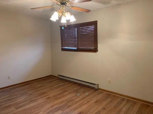 an empty room with wooden floor fan and windows
