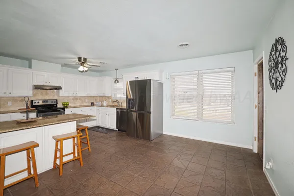 a kitchen with granite countertop a refrigerator a stove a sink a dining table and chairs