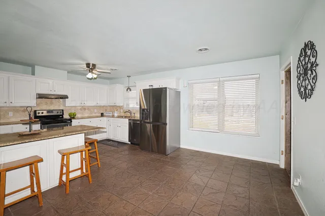 a kitchen with granite countertop a refrigerator a stove a sink a dining table and chairs