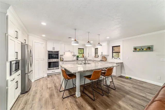 a kitchen with stainless steel appliances a dining table chairs stove refrigerator and wooden floor