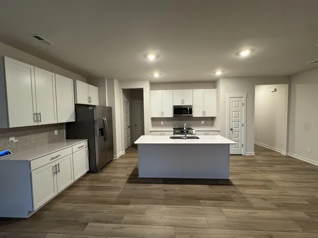 a large kitchen with a stove a sink dishwasher a refrigerator and white cabinets with wooden floor