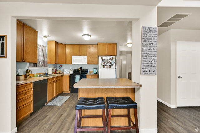 116 4th Street South Ogden, UT 84404 - Photo 4 of 7 Kitchen featuring wood-finish cabinetry, black appliances, light-toned countertops, a breakfast bar, and wood-look flooring