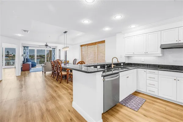 a kitchen with stainless steel appliances granite countertop a stove top oven a sink a dining table and chairs with wooden floor