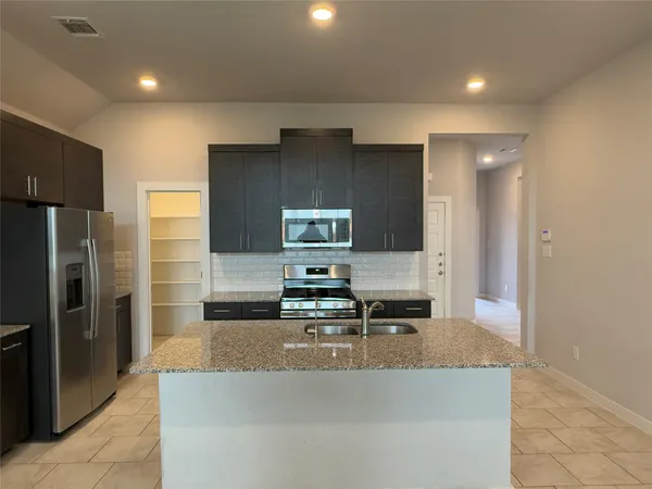 a kitchen with kitchen island granite countertop a refrigerator and a sink