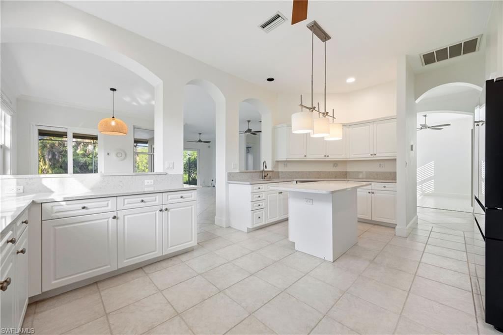 982 Fountain Run Naples, FL 34119 - Photo 10 of 44 Kitchen featuring white cabinets, a ceiling fan, arched walkways, and a kitchen island