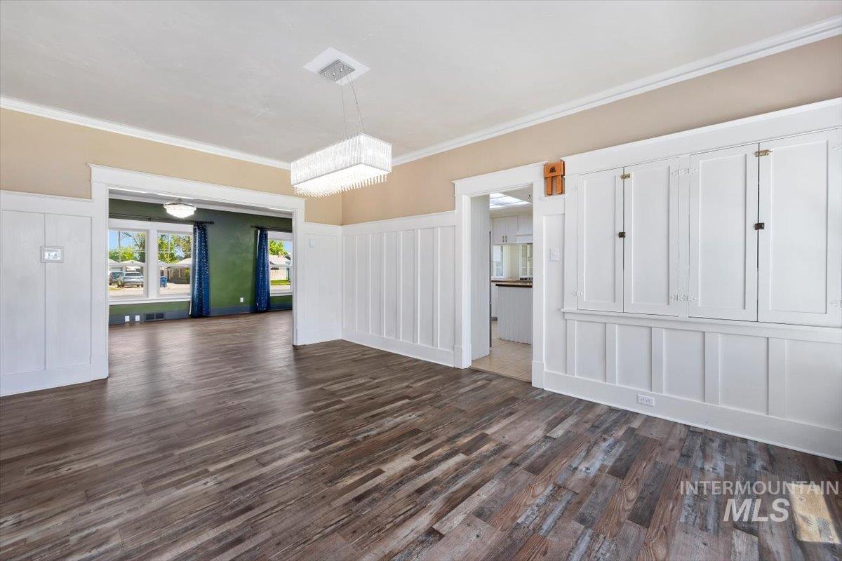 813 7th Street Rupert, ID 83350 - Photo 16 of 48 Spacious room featuring wood-finish flooring, white wainscoting, built-in cabinetry with dark hardware, and a contemporary rectangular pendant light fixture
