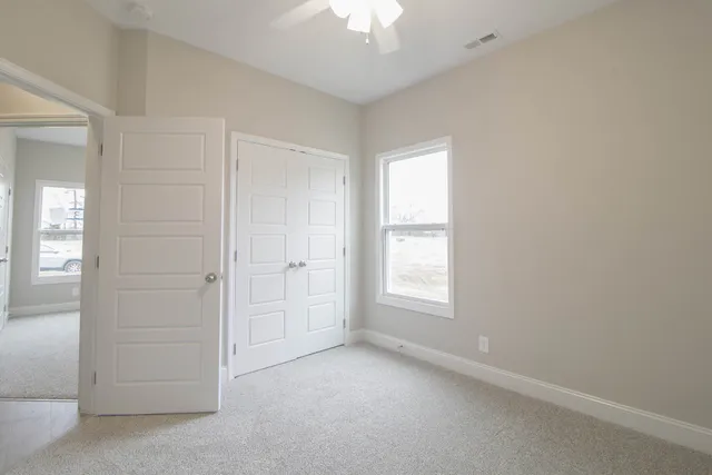 an empty room with chandelier fan and windows