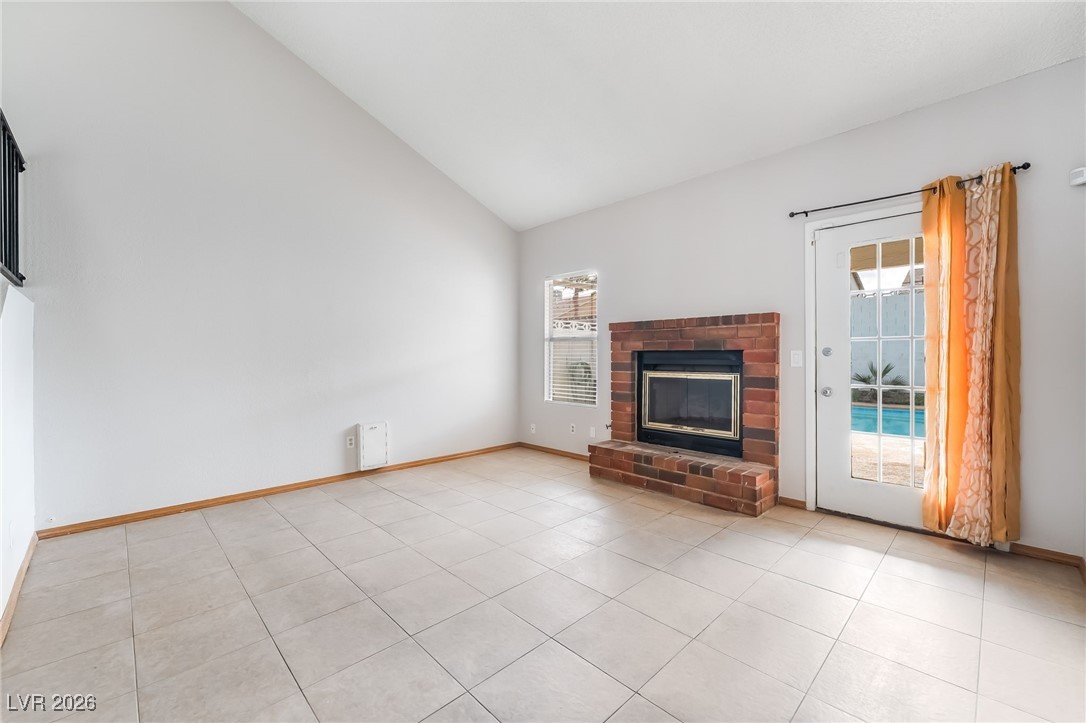 516 Inness Avenue Henderson, NV 89011 - Photo 12 of 42 Unfurnished living room with high vaulted ceiling, a brick fireplace, and light tile patterned floors