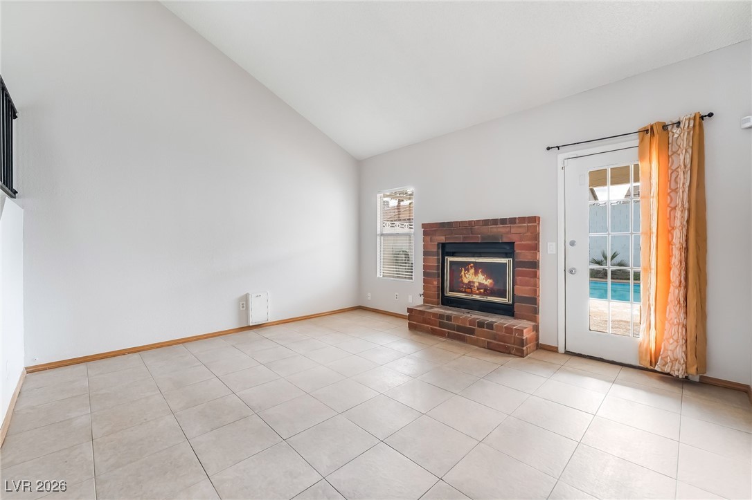 516 Inness Avenue Henderson, NV 89011 - Photo 13 of 42 Unfurnished living room with high vaulted ceiling, a brick fireplace, and light tile patterned floors