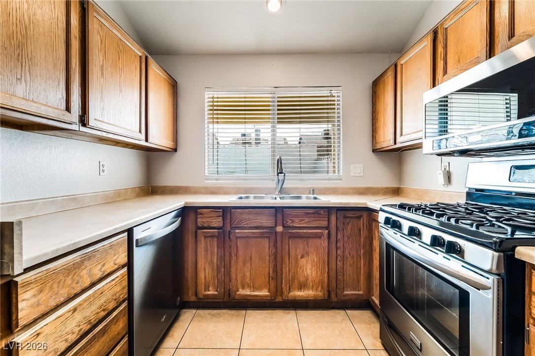 516 Inness Avenue Henderson, NV 89011 - Photo 16 of 42 Kitchen featuring stainless steel appliances, light countertops, light tile patterned floors, and brown cabinetry