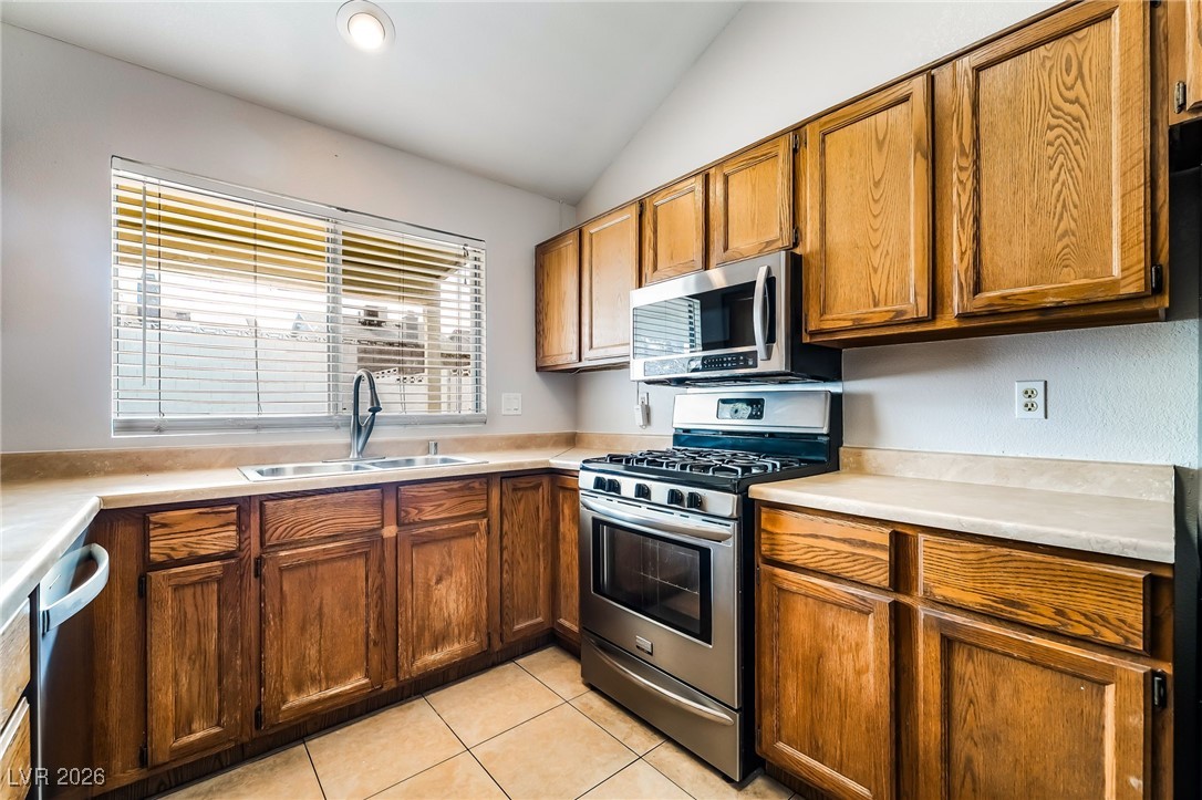 516 Inness Avenue Henderson, NV 89011 - Photo 17 of 42 Kitchen featuring stainless steel appliances, light countertops, brown cabinets, lofted ceiling, and light tile patterned floors