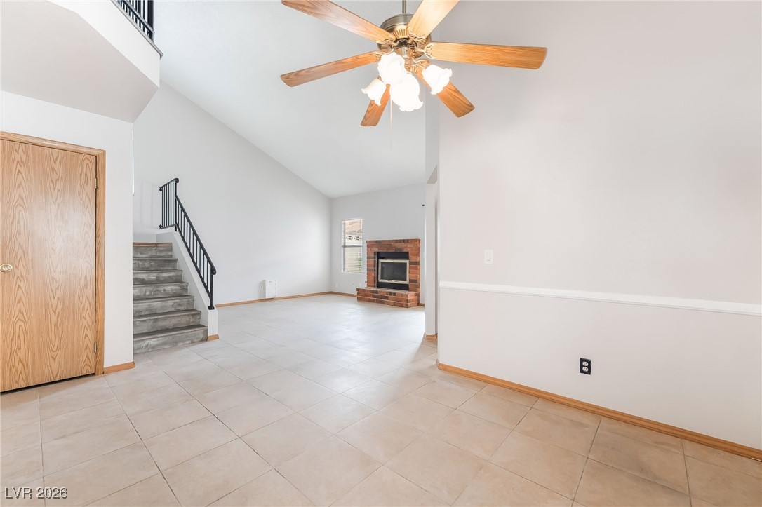516 Inness Avenue Henderson, NV 89011 - Photo 8 of 42 Unfurnished living room featuring stairway, a brick fireplace, high vaulted ceiling, light tile patterned flooring, and a ceiling fan
