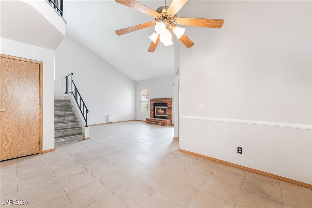 516 Inness Avenue Henderson, NV 89011 - Photo 9 of 42 Unfurnished living room with stairs, a fireplace, high vaulted ceiling, light tile patterned floors, and a ceiling fan