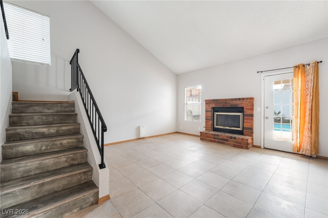 516 Inness Avenue Henderson, NV 89011 - Photo 10 of 42 Unfurnished living room with high vaulted ceiling, a fireplace, stairs, and light tile patterned flooring