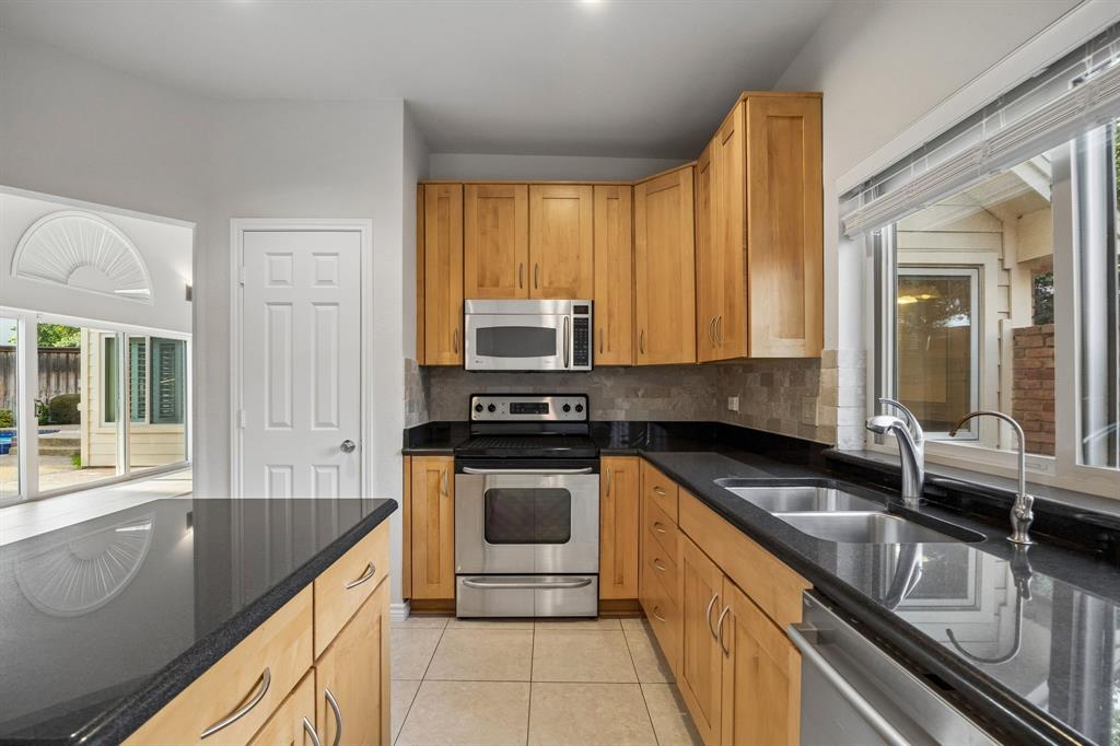 4115 Rive Lane Addison, TX 75001 - Photo 5 of 25 Kitchen featuring light wood cabinetry, black countertops, stainless steel appliances, and a tile backsplash