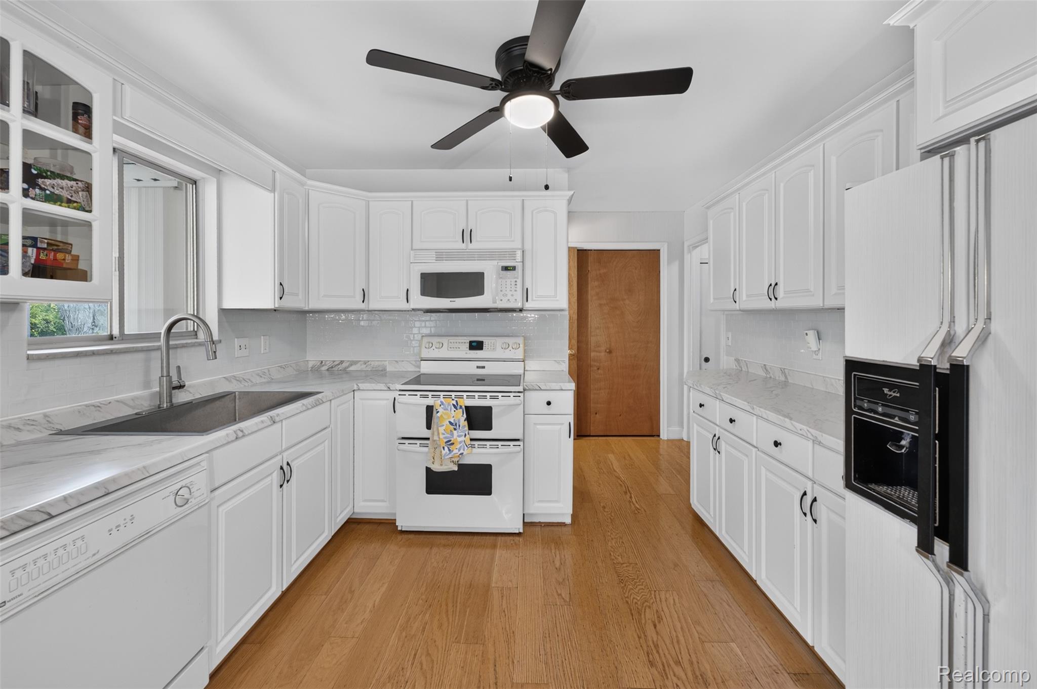 12055 West Pierson Road Flushing, MI 48433 - Photo 12 of 69 White cabinetry, light-toned countertops, tile backsplash, wood-finish flooring, and white appliances