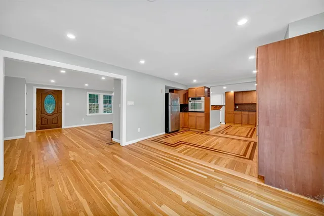 a view of an empty room with wooden floor and kitchen
