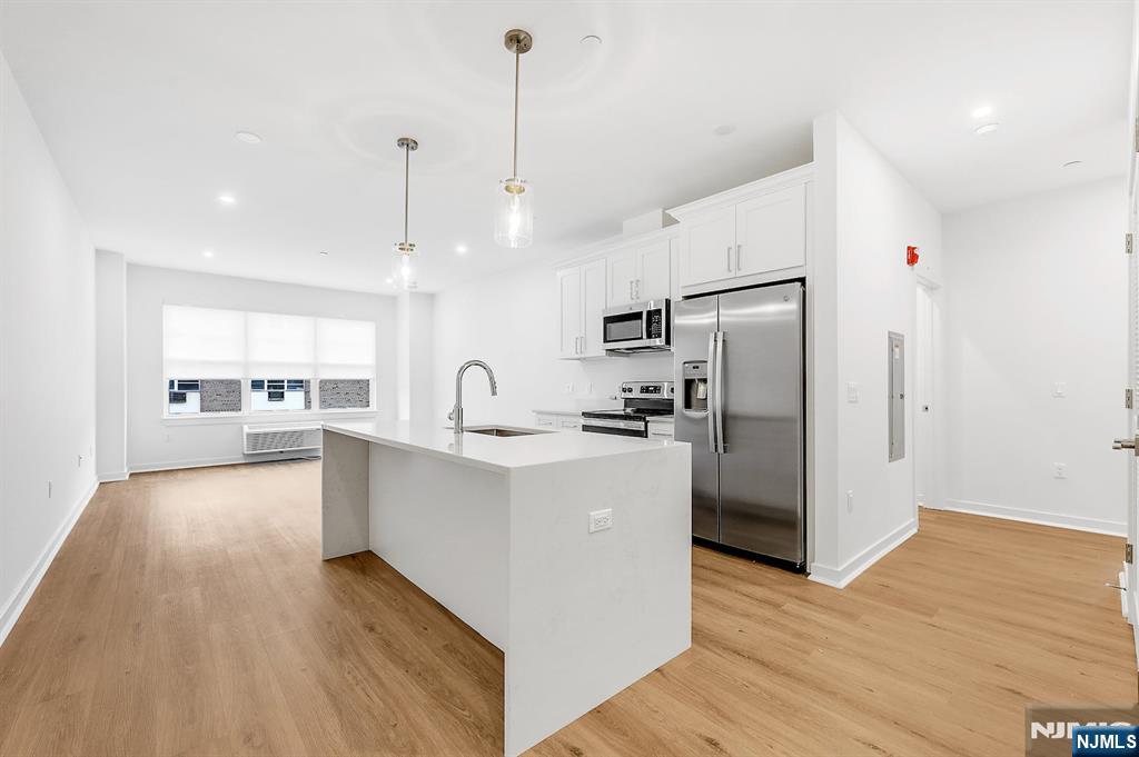 a large kitchen with stainless steel appliances a refrigerator a sink dishwasher a oven and white cabinets with wooden floor