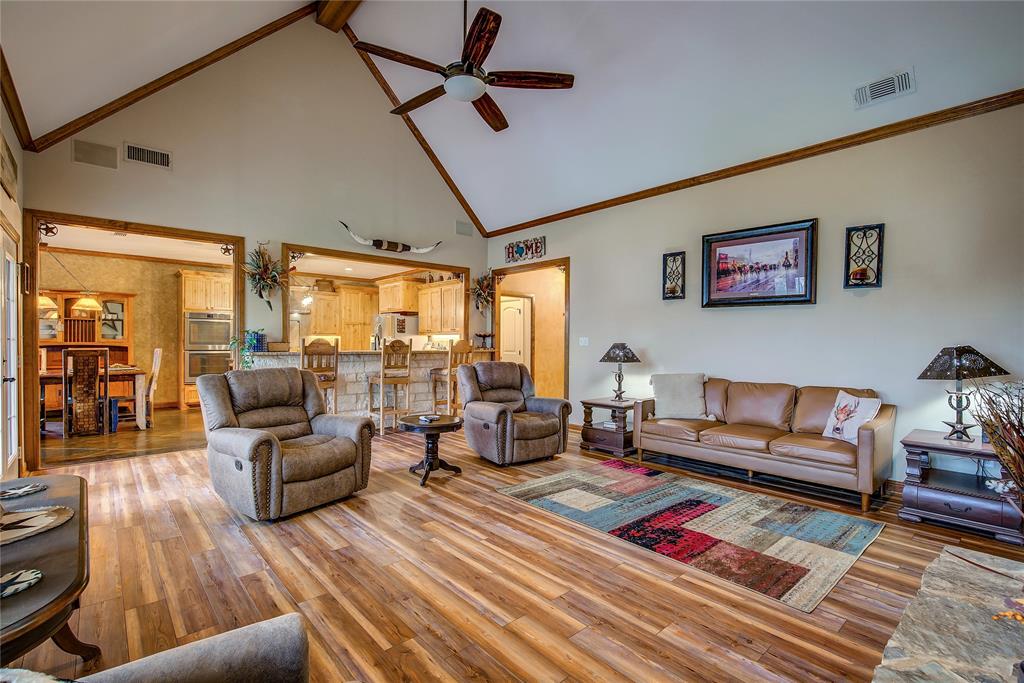 811 County Road 4250 Point, TX 75472 - Photo 15 of 38 Living room featuring soaring ceilings, a stone wood-burning fireplace, newly finished wood flooring, and large windows that fill the space with natural light and beautiful countryside views.
