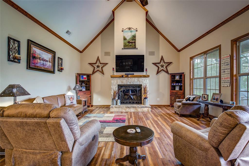 811 County Road 4250 Point, TX 75472 - Photo 16 of 38 Living room featuring soaring ceilings, a stone wood-burning fireplace, newly finished wood flooring, and large windows that fill the space with natural light and beautiful countryside views.