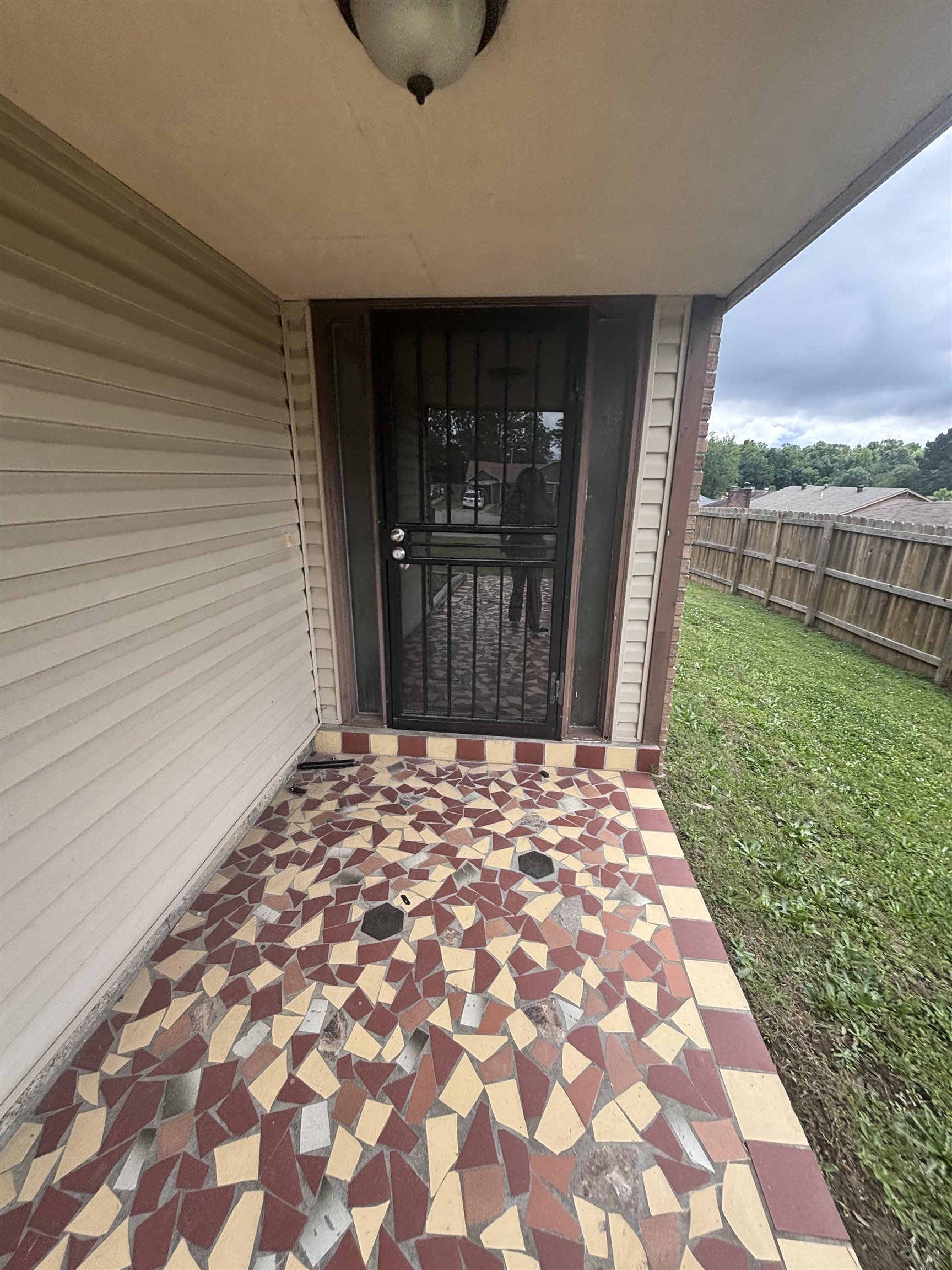 3021 Meadowfair Road Memphis, TN 38118 - Photo 2 of 3 Covered porch featuring a mosaic tile floor, beige vinyl siding, a black security screen door, and a traditional ceiling light fixture