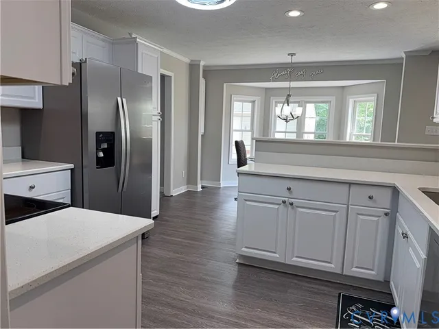 a kitchen with stainless steel appliances granite countertop a refrigerator a sink and white cabinets with wooden floor
