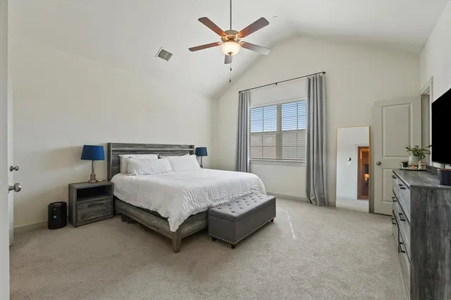 a spacious bedroom with a bed and a flat tv screen on dresser
