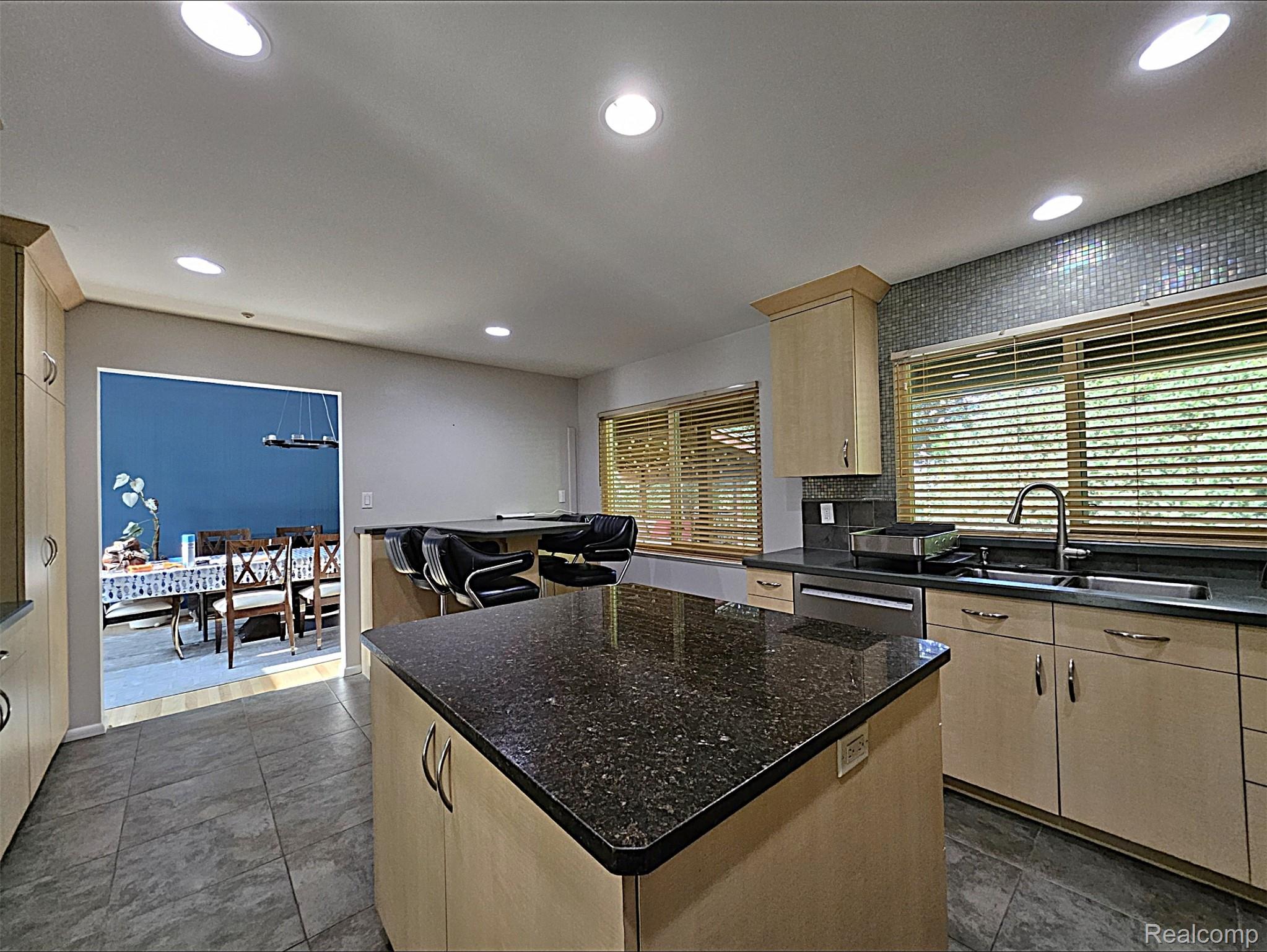 7120 Pebblecreek Road West Bloomfield, MI 48322 - Photo 17 of 31 Spacious kitchen featuring a large island with dark stone countertop, light wood-finish cabinetry, tile flooring, and a mosaic tile backsplash