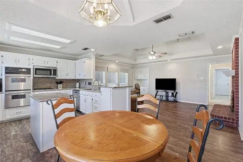 a living room with stainless steel appliances kitchen island granite countertop a stove a dining table and chairs with wooden floor