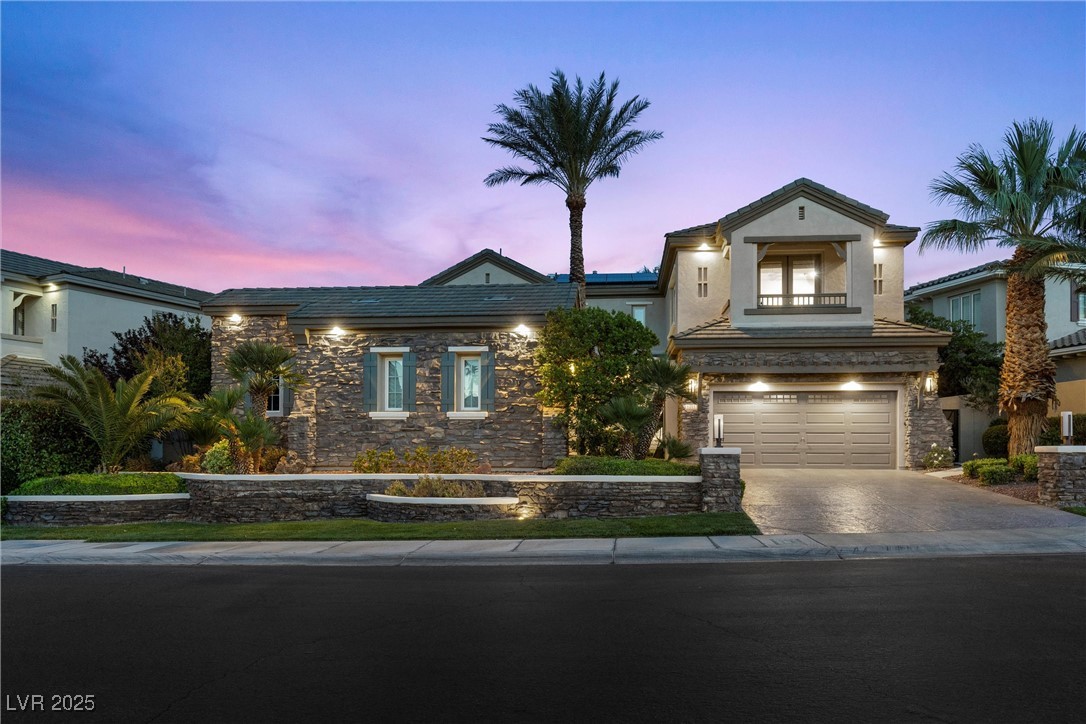 View of front of property featuring an attached garage, concrete driveway, stucco siding, and stone siding