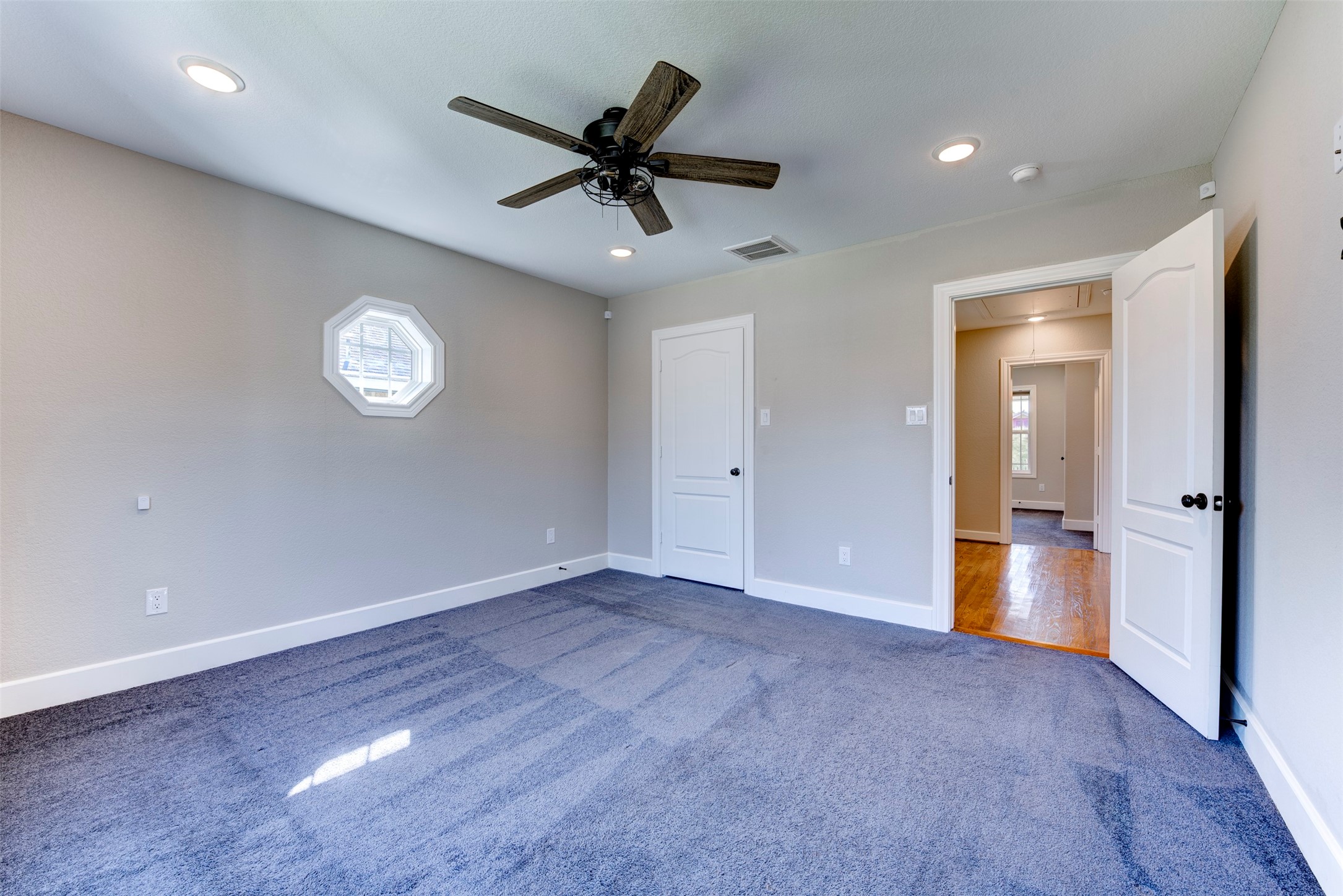 109 Dresden Street Houston, TX 77012 - Photo 37 of 43 Another view features fresh carpet, neutral walls, a ceiling fan, recessed lighting, and a unique octagonal window. It connects to a hallway with hardwood flooring, enhancing its modern, airy feel.