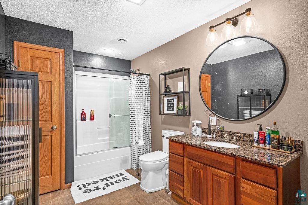 2783 Lauren Road Duluth, MN 55804 - Photo 14 of 47 Bathroom featuring vanity, shower / bath combination with glass door, a textured wall, a textured ceiling, and light tile patterned floors