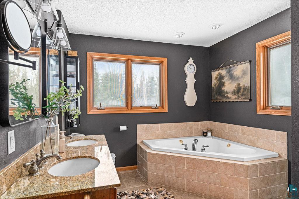 2783 Lauren Road Duluth, MN 55804 - Photo 24 of 47 Full bath with double vanity, a bath, a textured ceiling, and light tile patterned flooring