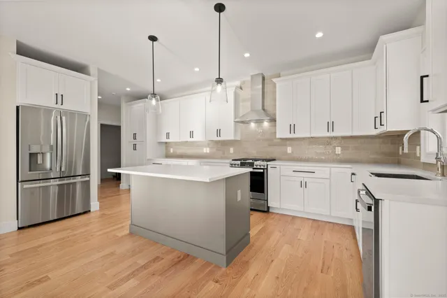 a large kitchen with stainless steel appliances granite countertop a refrigerator a sink dishwasher a stove and white countertops with wooden floor