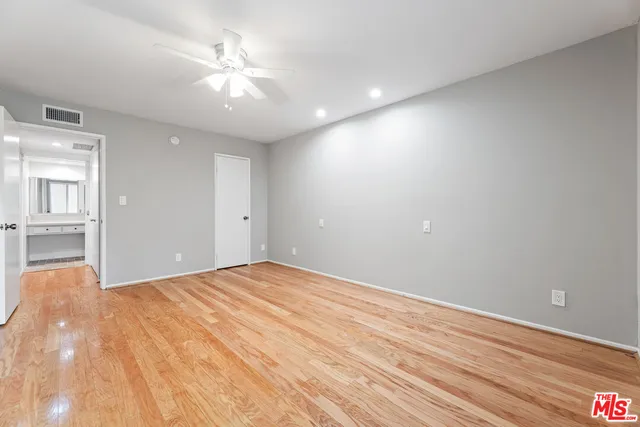 a view of an empty room with wooden floor and a ceiling fan