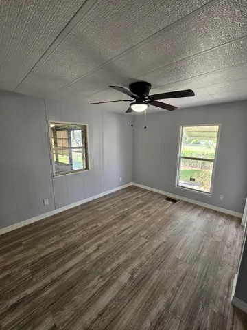 an empty room with wooden floor fan and windows