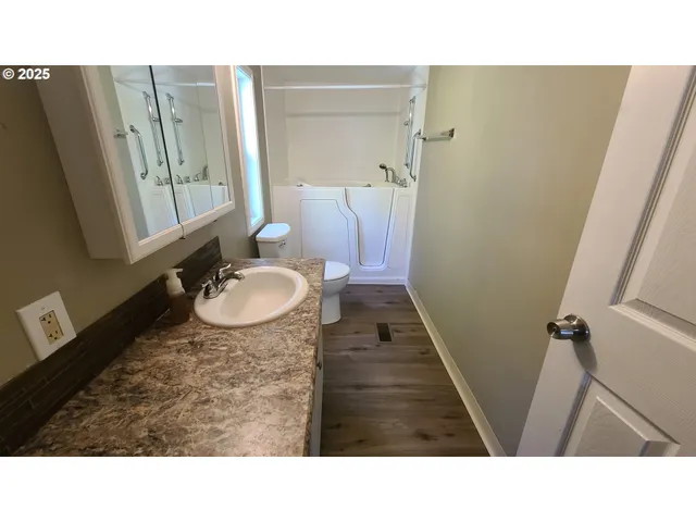 a living room with stainless steel appliances kitchen island granite countertop a refrigerator a stove and a sink with wooden floor