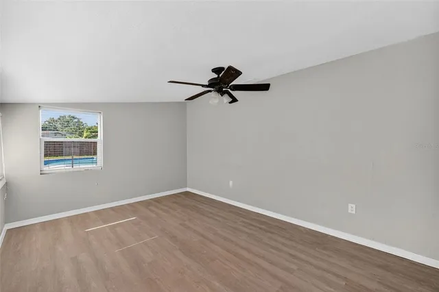an empty room with wooden floor ceiling fan and window