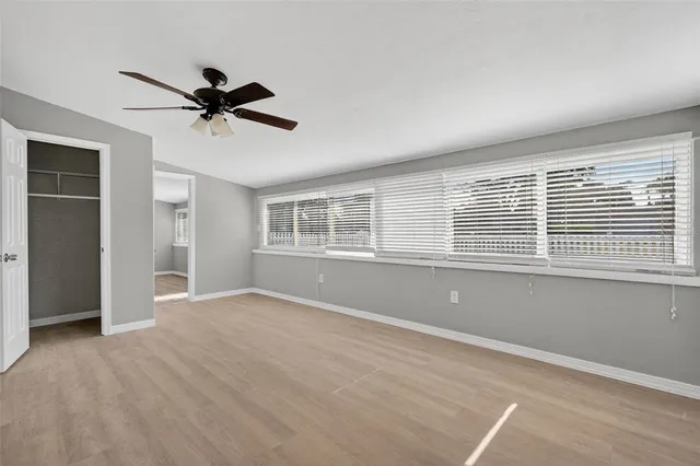 an empty room with wooden floor ceiling fan and windows