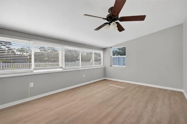 an empty room with wooden floor ceiling fan and windows