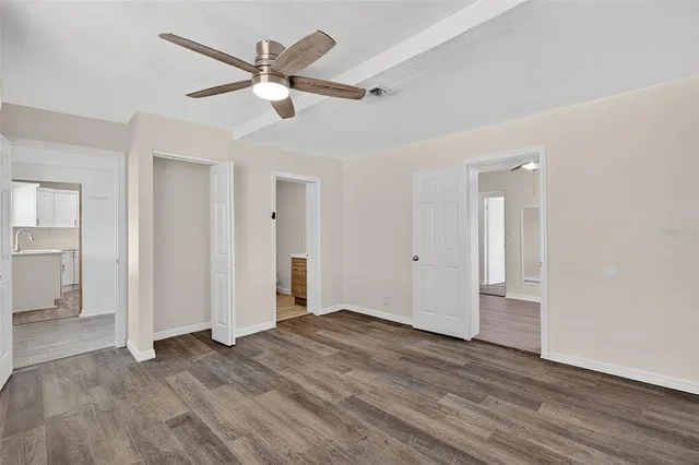 a view of an empty room with wooden floor and a ceiling fan