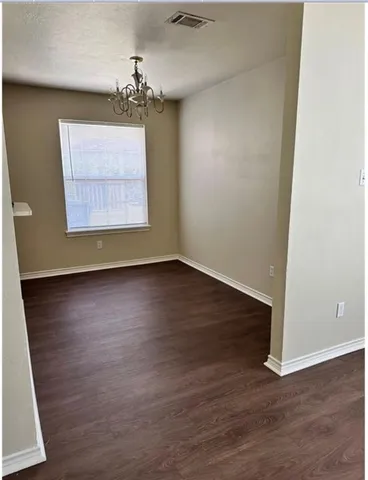 an empty room with wooden floor chandelier and windows