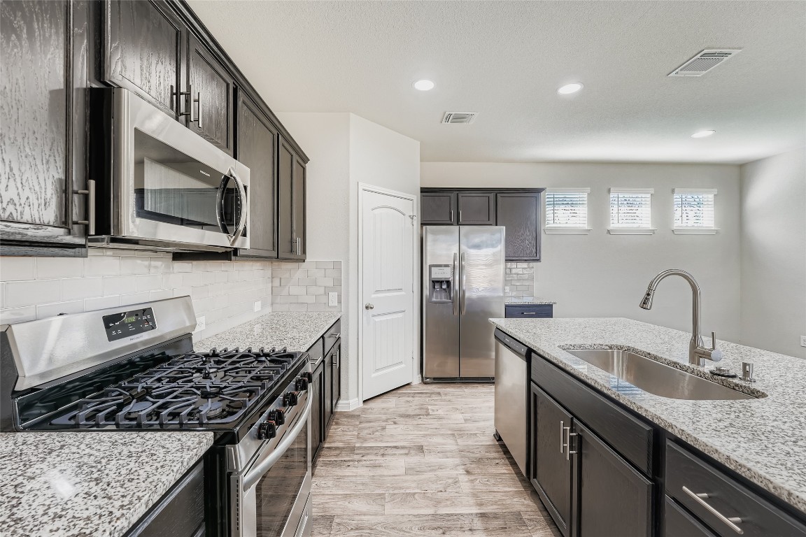 14601 Frankel Loop Pflugerville, TX 78660 - Photo 4 of 17 Kitchen with stainless steel appliances, light wood-style flooring, light stone countertops, recessed lighting, and decorative backsplash