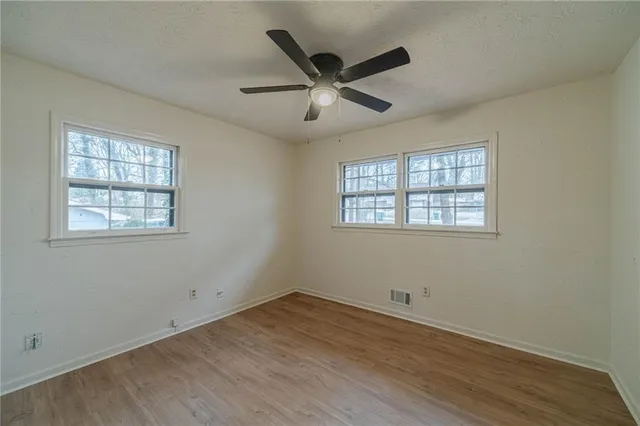 an empty room with wooden floor ceiling fan and windows