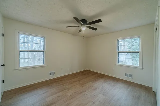 an empty room with wooden floor ceiling fan and windows