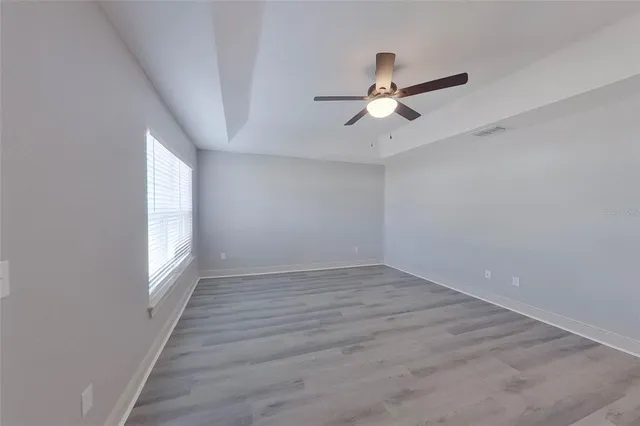 an empty room with wooden floor fan and windows